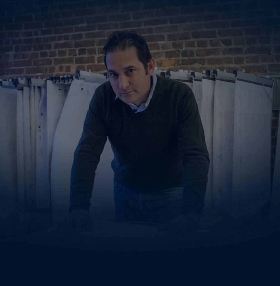 Boaz Gilad reviewing architectural plans in a brick-walled studio
